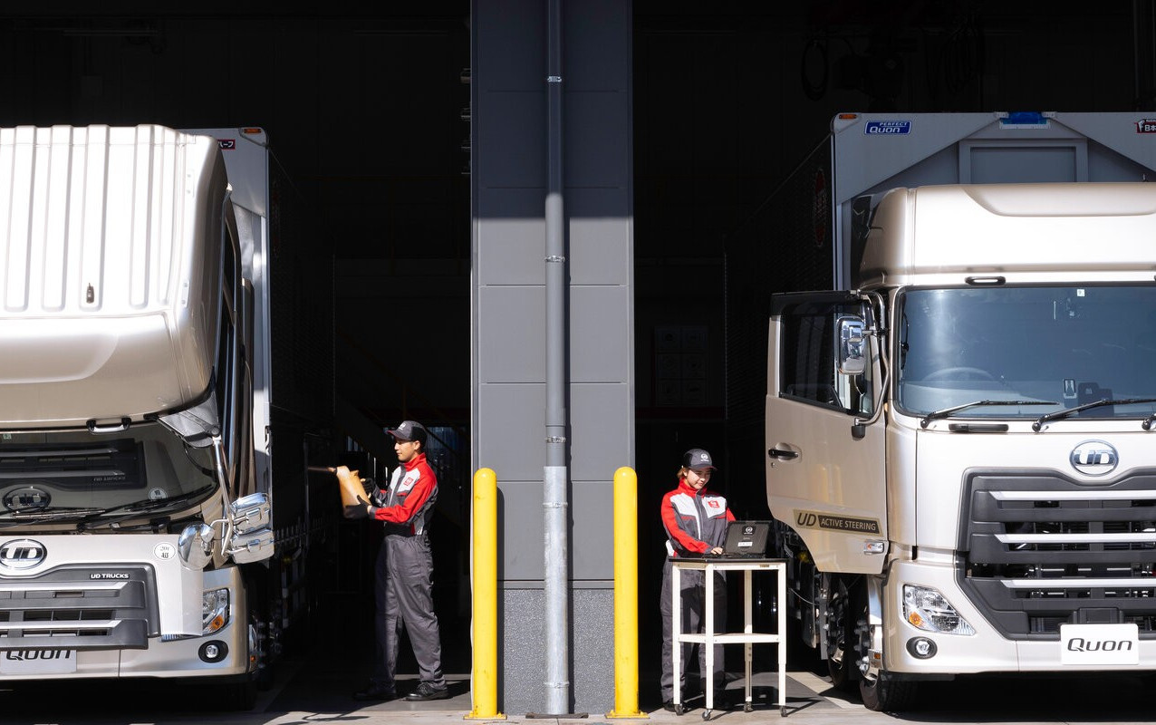 Two workers in red uniforms beside parked delivery trucks in a loading area.
