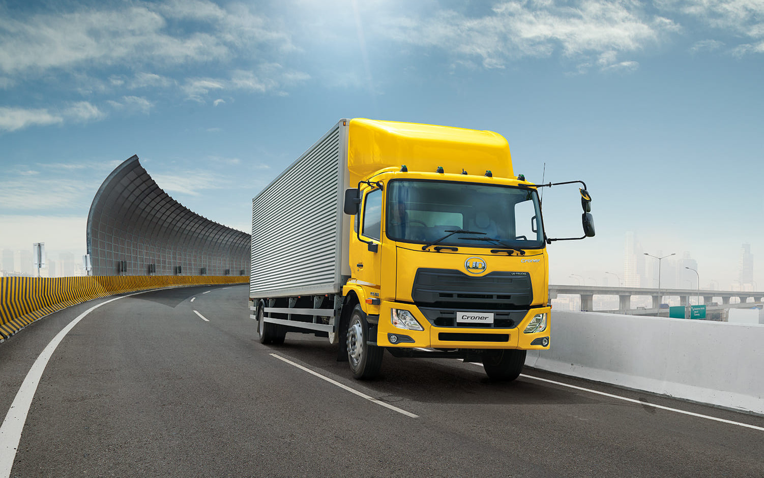 Yellow truck driving on a curved highway under a blue sky.