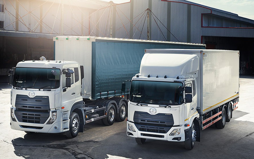 Two white cargo trucks parked outside a warehouse in daylight.