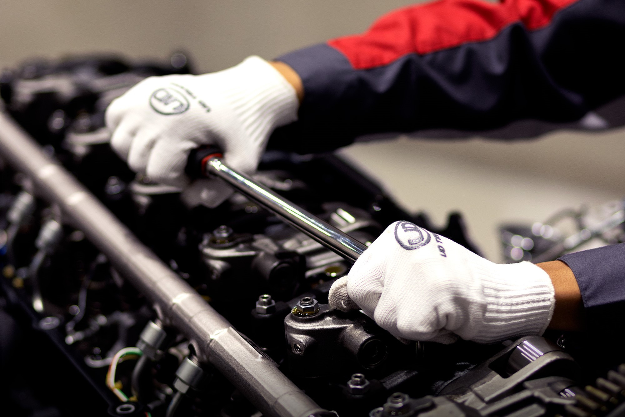 Mechanic using a wrench to work on an engine while wearing white gloves.