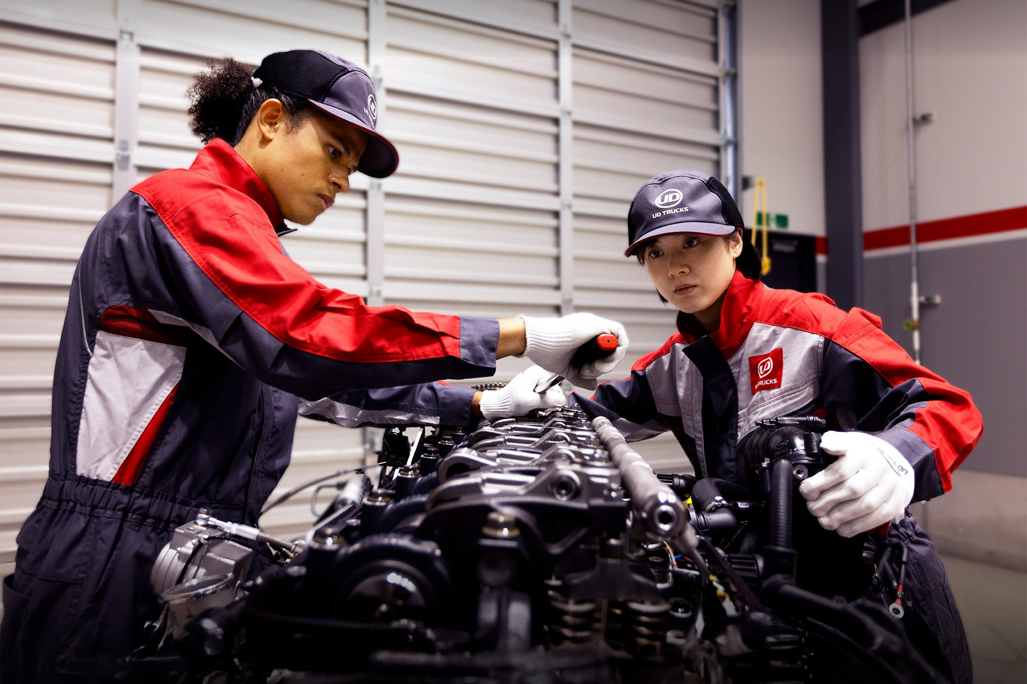 Two mechanics in uniforms working on a large engine in a garage.