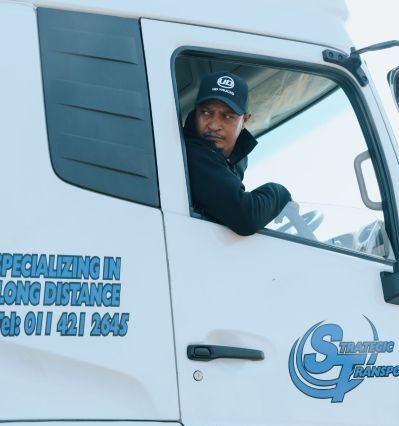Man in a truck cab looking out the window, wearing a dark cap.