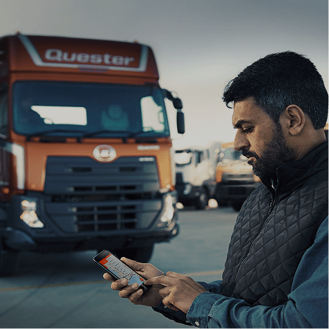 Man using smartphone near a red truck in a parking lot.