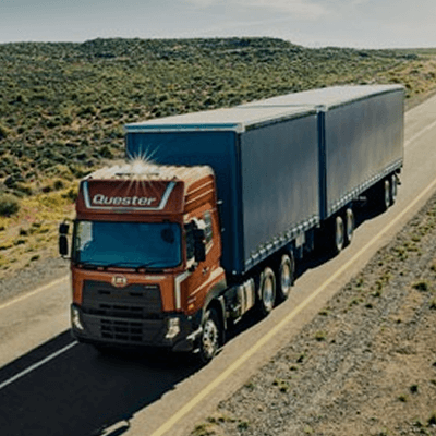 Lori kargo besar berwarna merah dan biru di jalan raya terbuka.