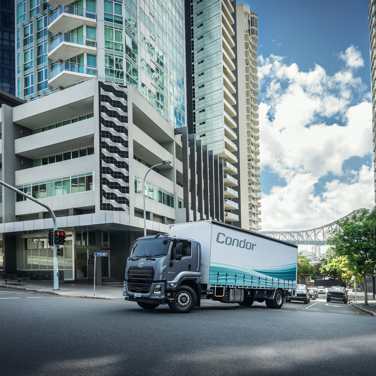 Delivery truck turning at city intersection with high-rise buildings and partly cloudy sky.
