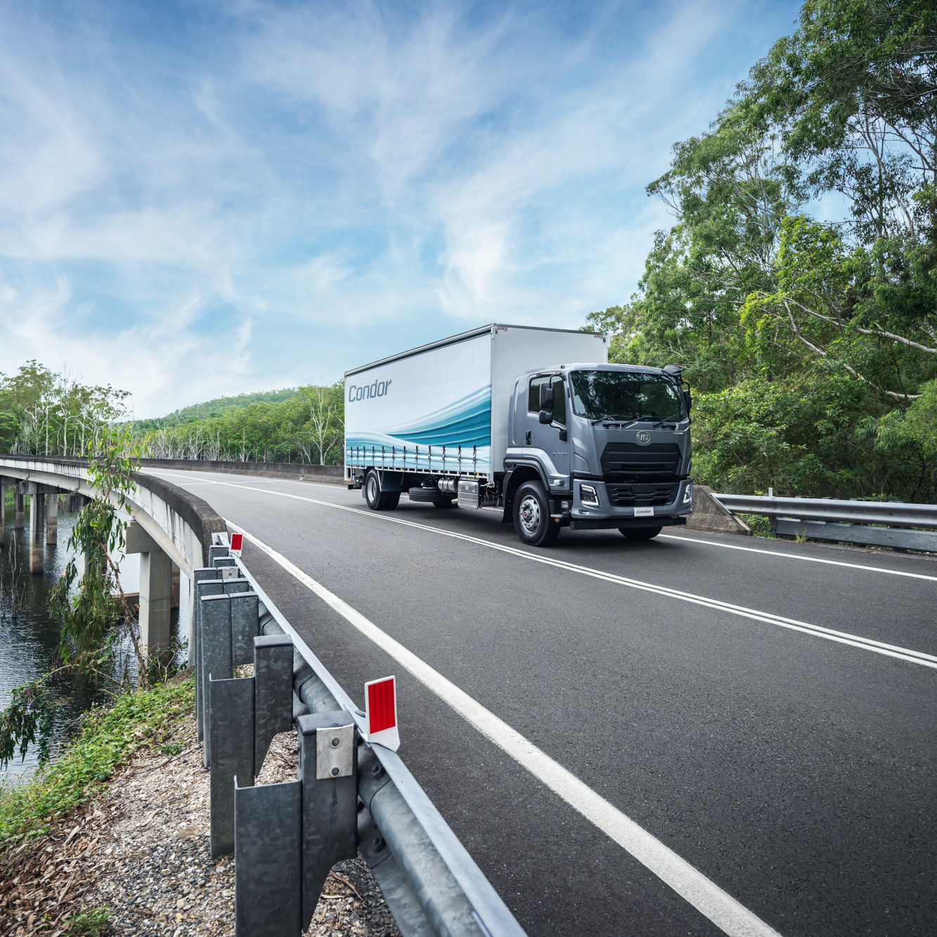 Truck driving on a curved road through green trees under a blue sky.