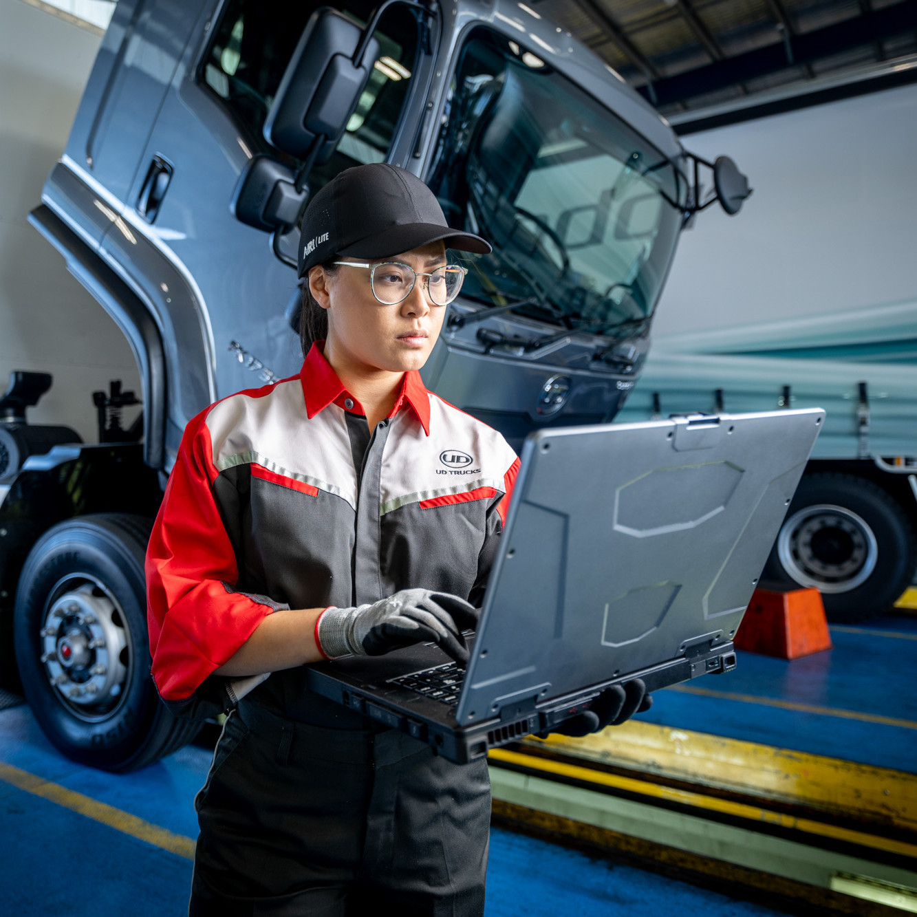 Mechanic in uniform using a laptop near a large truck in a workshop.