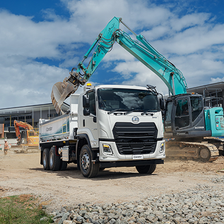 Excavator loading dirt into white tipper truck at construction site under blue sky