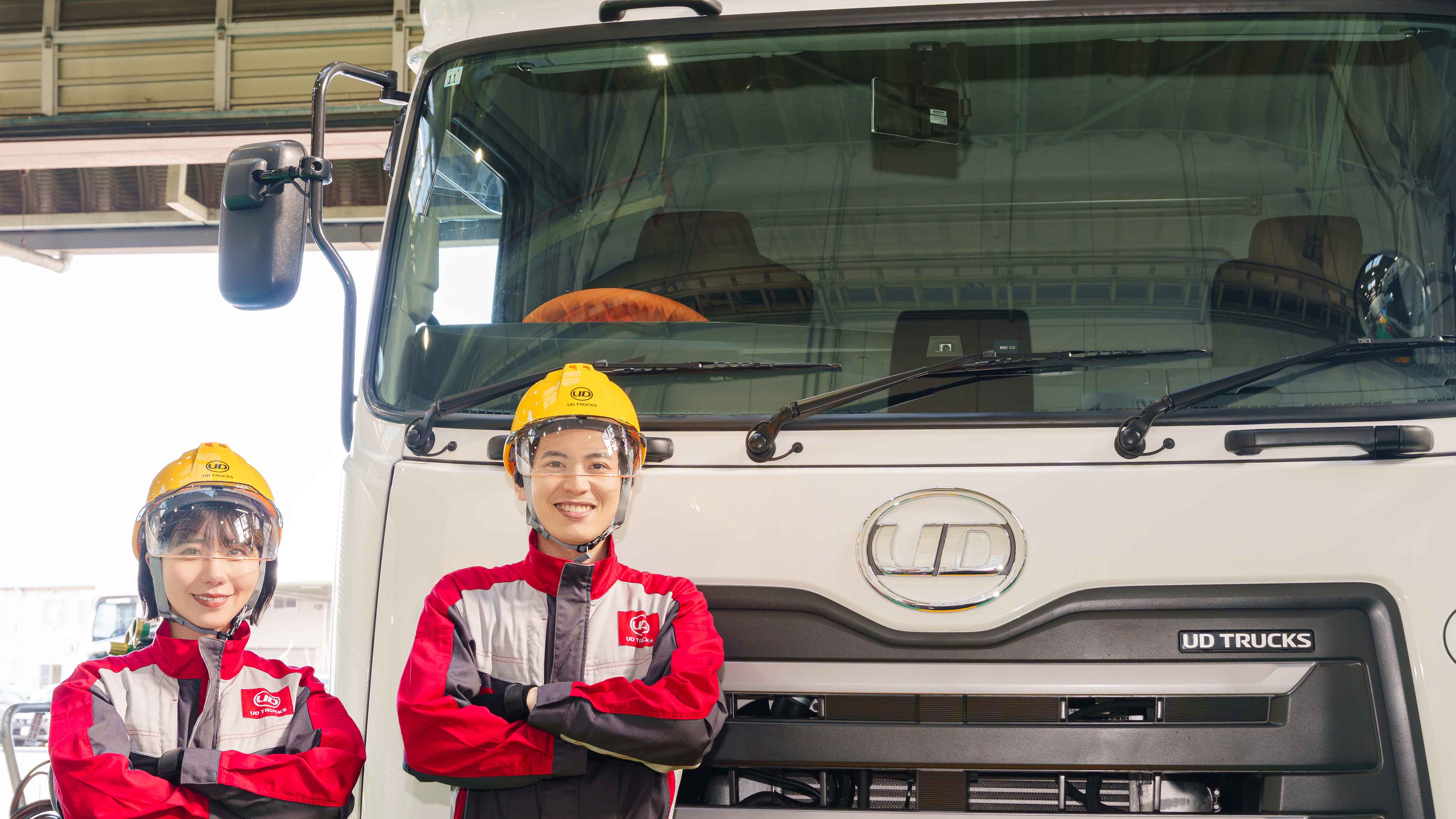 作業着とヘルメットを着た2人が大型トラックの前で笑顔
