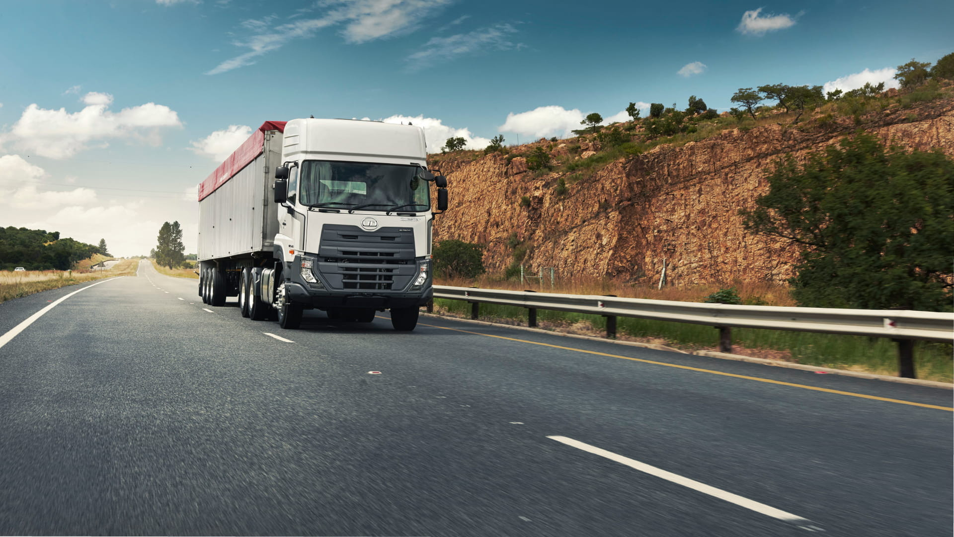 شاحنة كبيرة تسير على طريق سريع بجانب جرف صخري في يوم مشمس