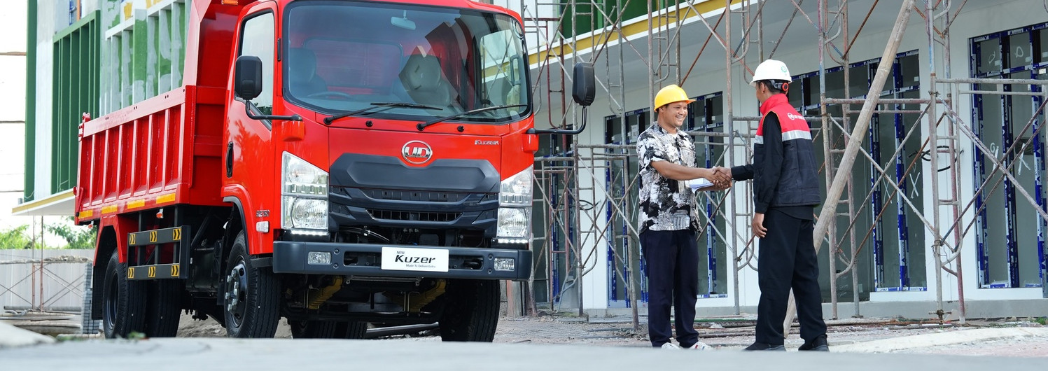 Two workers shake hands near a red truck at a construction site with scaffolding.