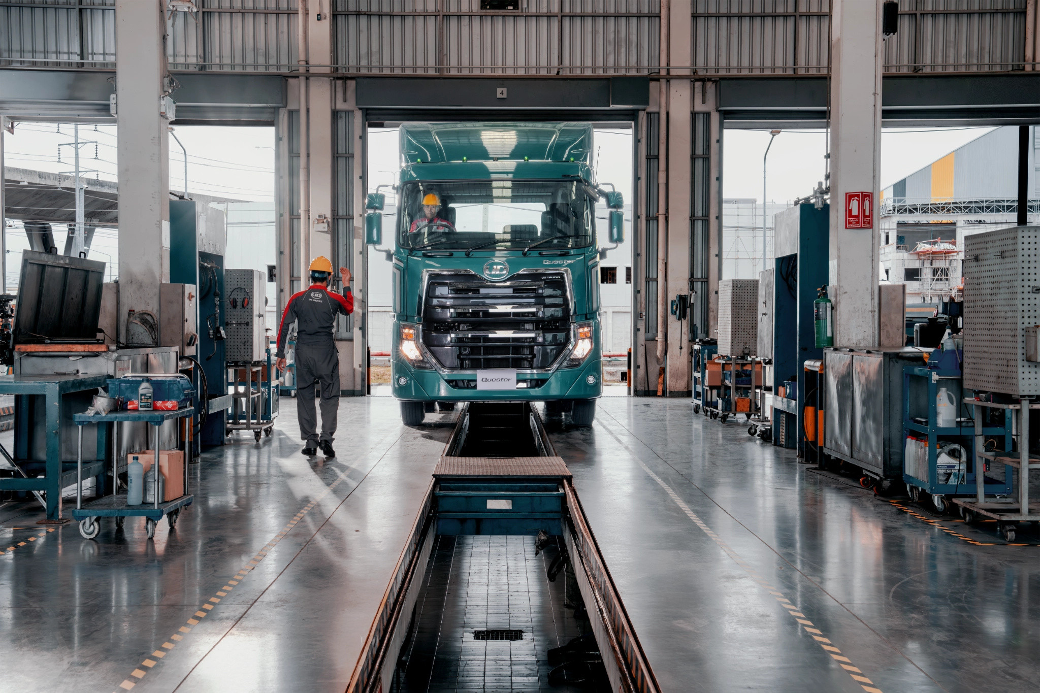 Large green truck inside a spacious garage, workers inspecting and maintaining vehicles.