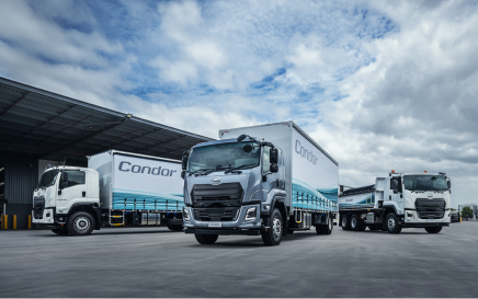 Three large Condor trucks parked outside a warehouse under cloudy skies.