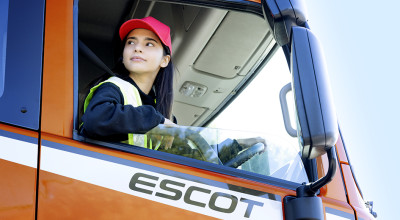 Woman in red cap and safety vest driving an orange truck labeled ESCOT.