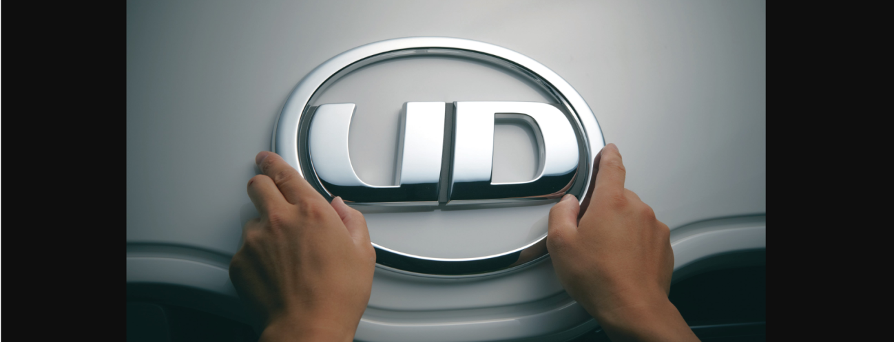 両手で触れられているUDロゴの車のエンブレム