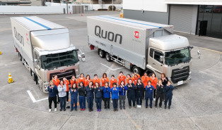 二台の大型トラックの前で並んでポーズをとる作業員たち