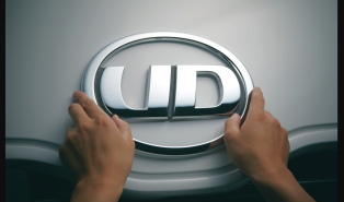 車のフロントにあるUDトラックスのロゴを両手で持っている様子