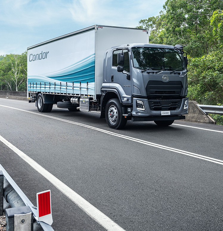 Grey delivery truck driving on a highway surrounded by green trees
