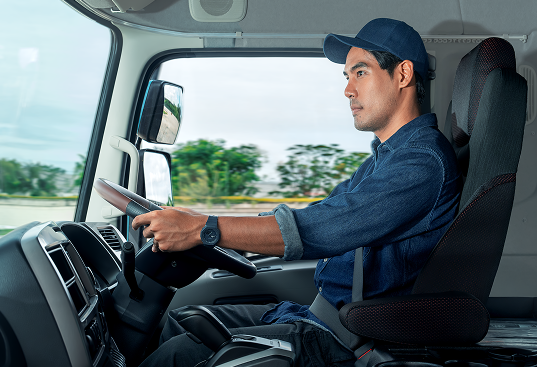 Man driving a truck, wearing a blue cap and denim shirt, focused on the road.