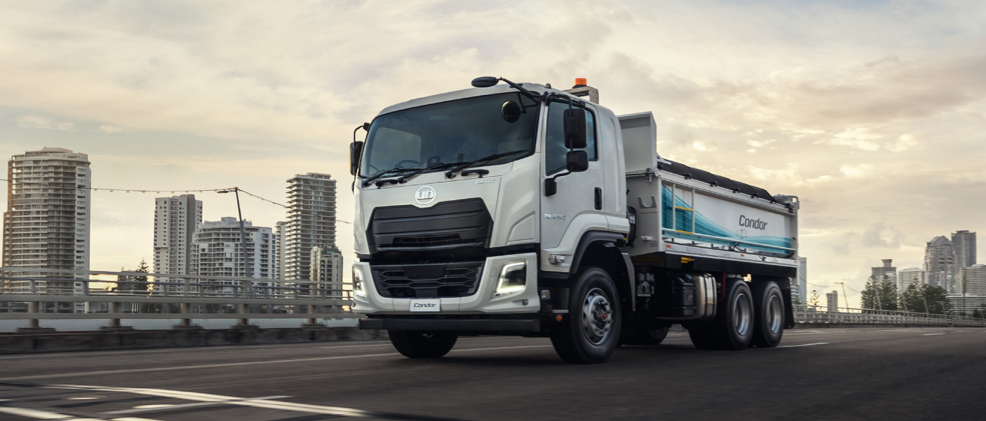 White dump truck parked on a city street with tall buildings in the background.